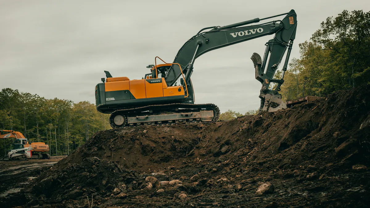 Orange and grey tracked excavator working on an earth embankment at a construction site.