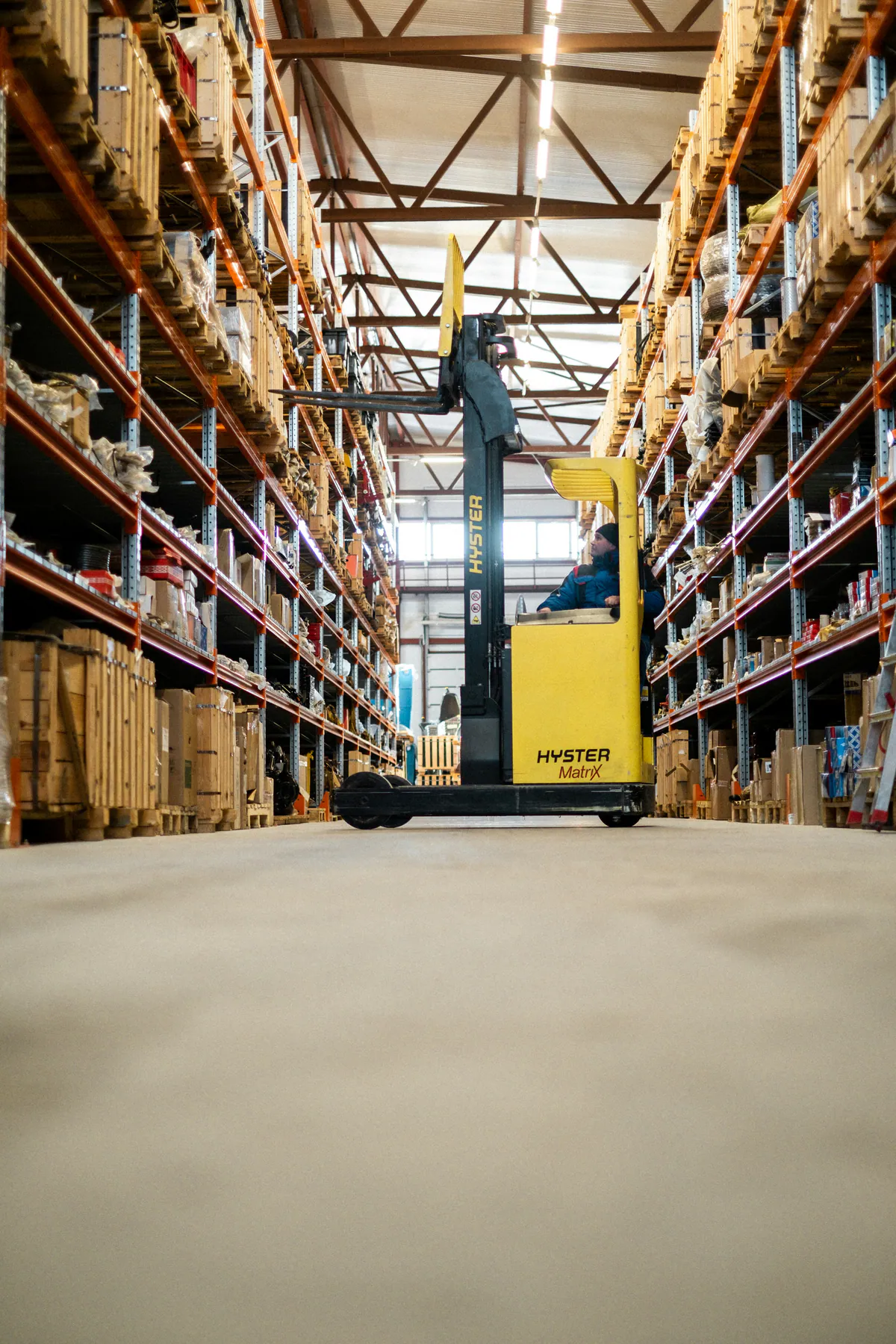 Yellow reach truck moving between tall racks of boxed inventory in a warehouse.