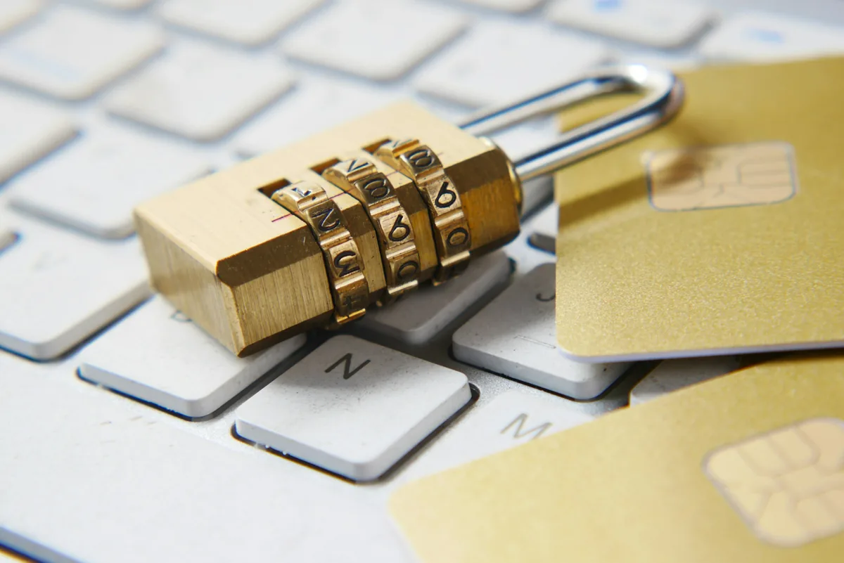 A brass combination padlock and payment cards resting on a white computer keyboard.