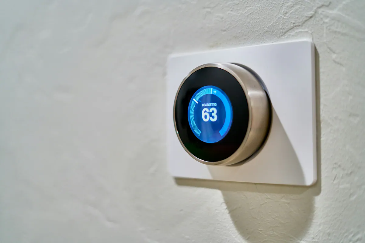 Wall-mounted smart thermostat showing 63 degrees in a home interior.